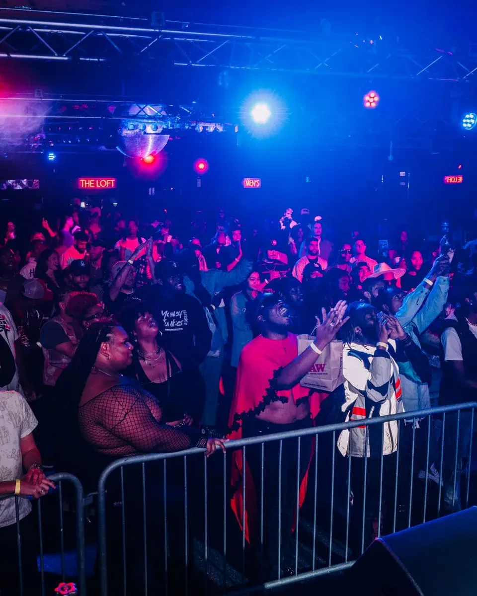 A packed room at a Something Dope open mic, the crowd pressed against the barrier with hands in the air
